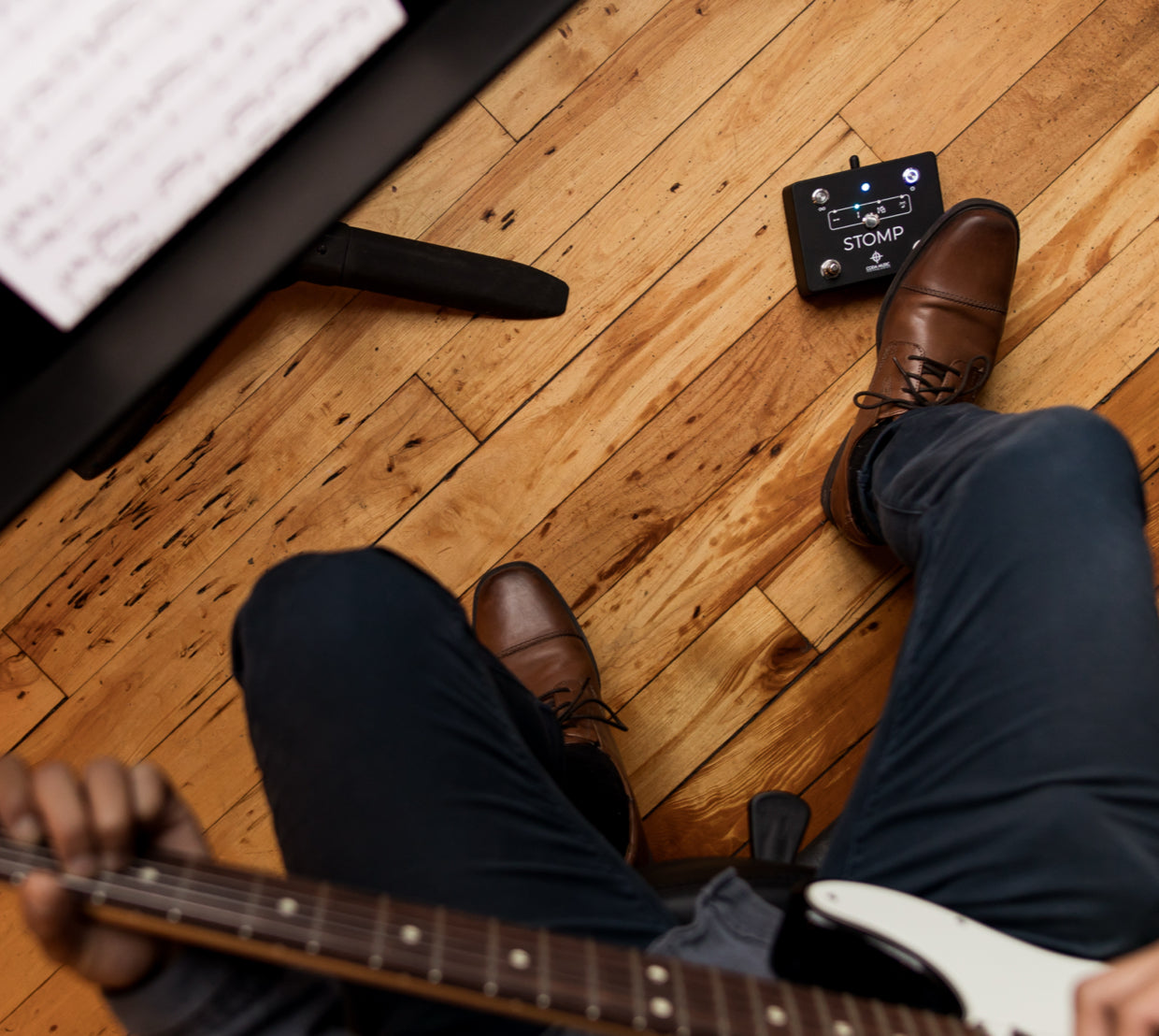 Person playing guitar on a wooden floor with a keyboard and effects pedal.