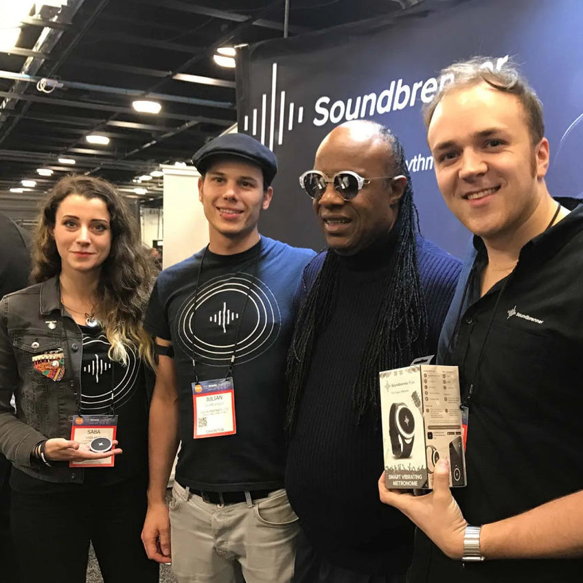 四个人站在 Soundbrenner 展位前，其中一人拿着产品包装盒