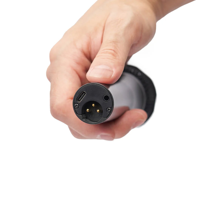 Hand holding a black cylindrical device with a round multi-pin connector