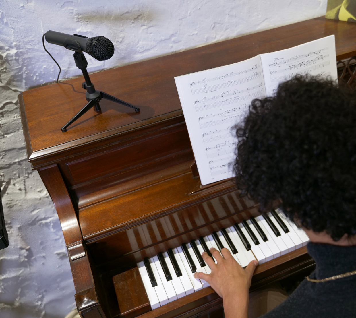 Person playing an upright piano with a microphone positioned above it