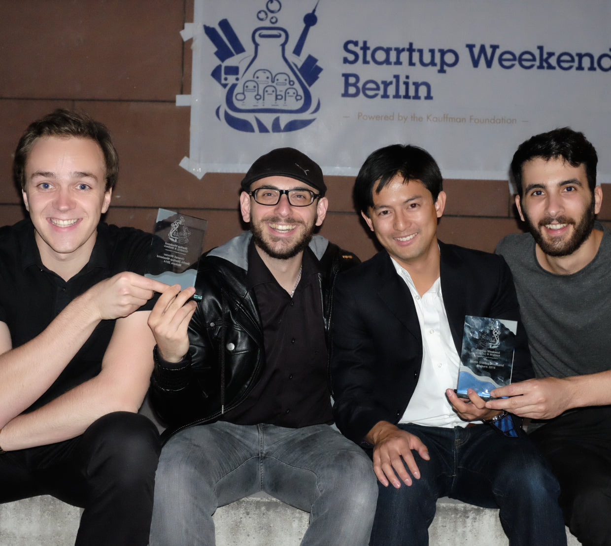 四名男子坐在Startup Weekend Berlin标牌下方