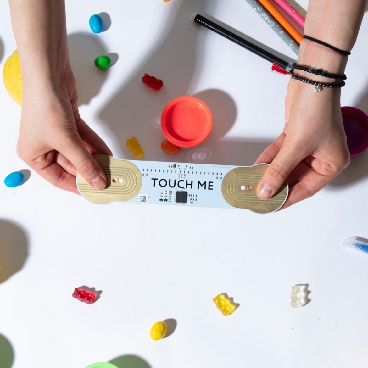 双手在摆放着彩色物体的桌面上方握着 TouchMe MIDI 乐器